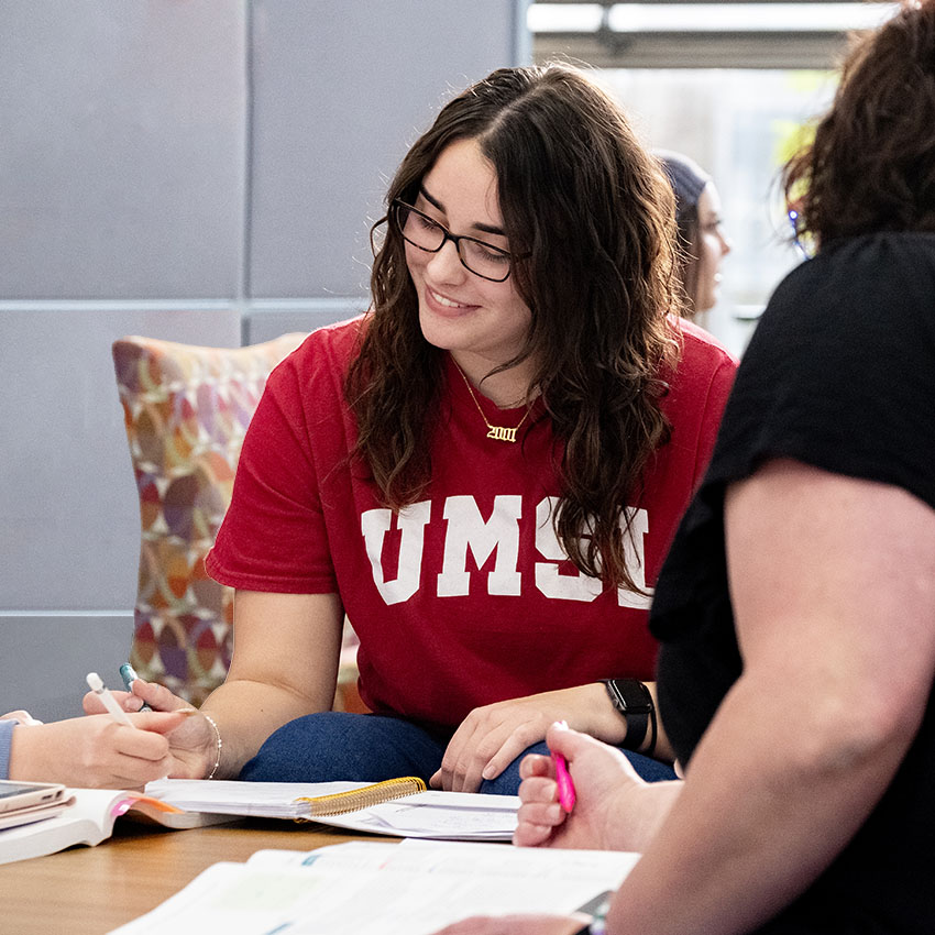 An umsl student wearing a red UMSL t-shirt engages in a collaborative study session with peers.